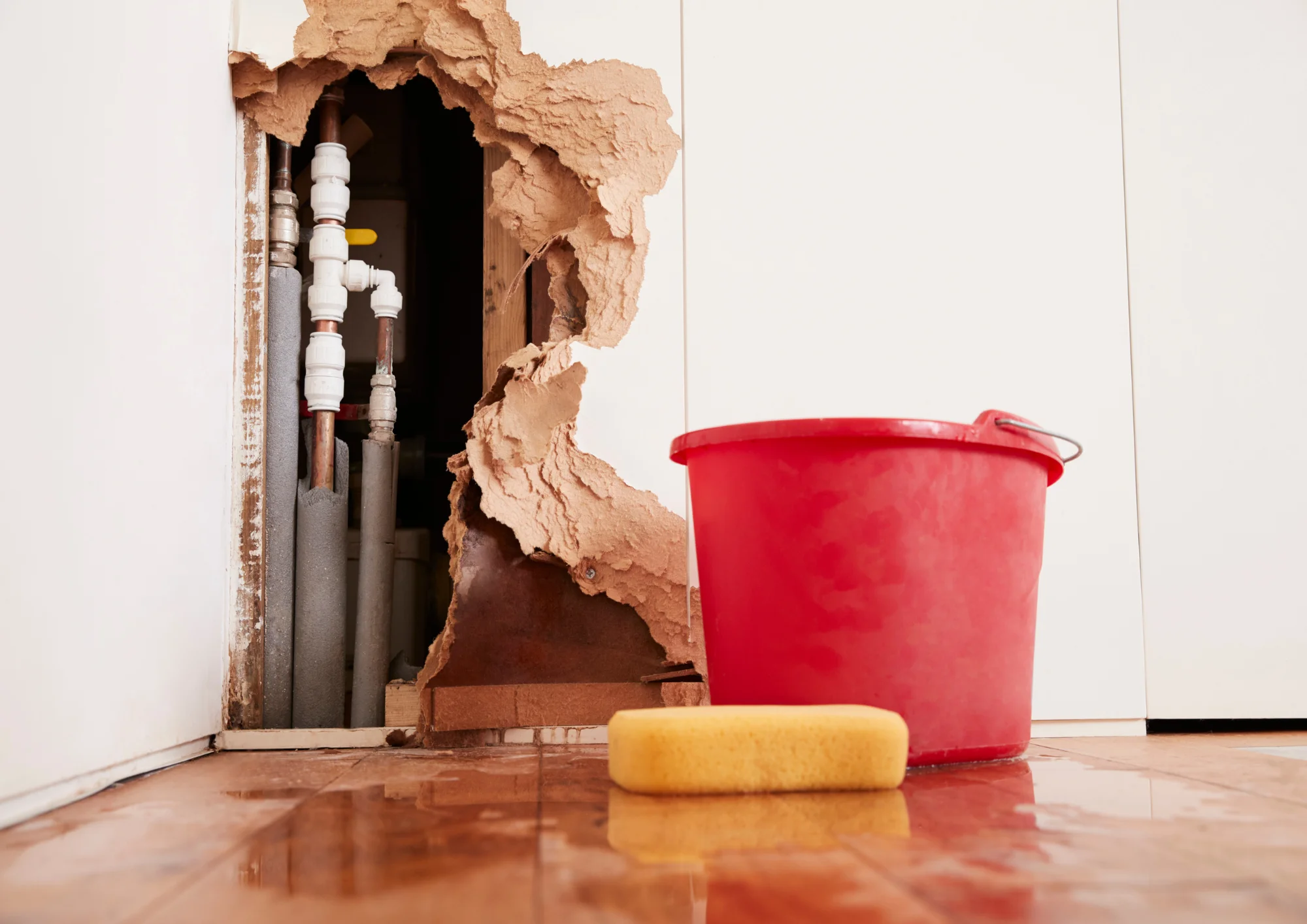 Exposed burst water pipe behind a damaged wall with sponge and bucket, showing signs of a hidden leak — Rockwall Plumbing
